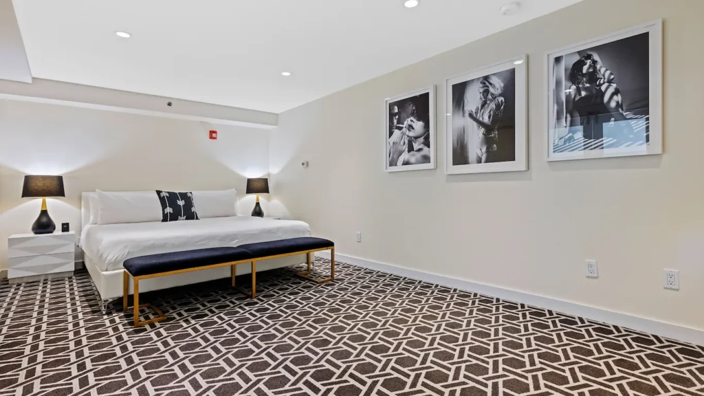 A wide view of a hotel room with a large bed, bench, nightstands, and black and white artwork.
