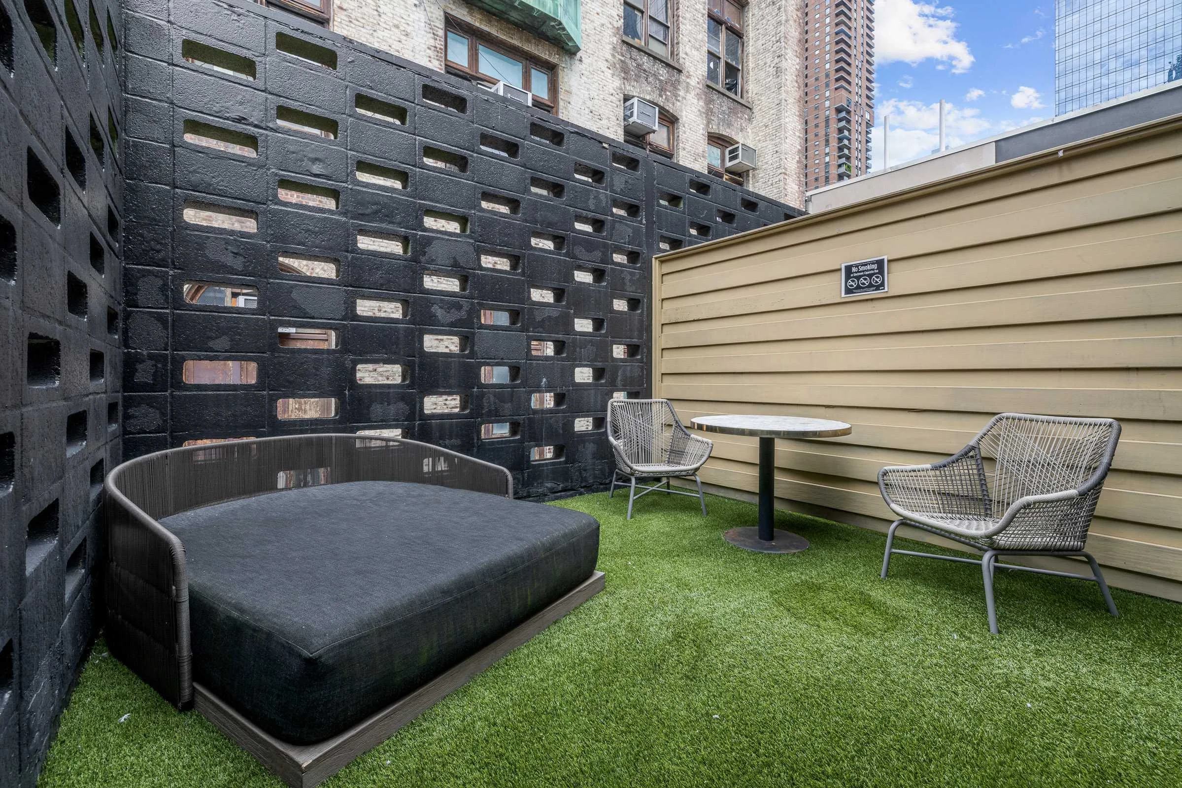 A small rooftop garden with artificial turf, outdoor seating, and a privacy screen.